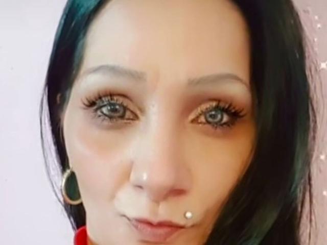 Brighy's face with black hair, blue eyes, long eyelashes, and a small beauty mark below her right lip. She's wearing a headset and a red shirt.
