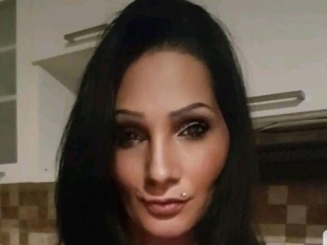 Brighy's face with dark brown hair, brown eyes, and a small lip piercing. She's smiling slightly, with a subtle nose and full lips. Her skin is light brown.