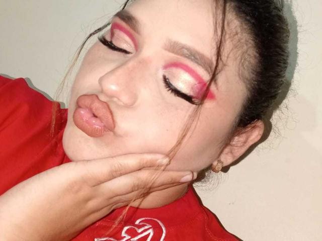 ChubbyKinkyWoman with pouty lips, pink and white eye makeup, red shirt, hand on cheek, brown hair, gold earrings, eyes closed, soft skin, slight blush, full lips, head tilted.