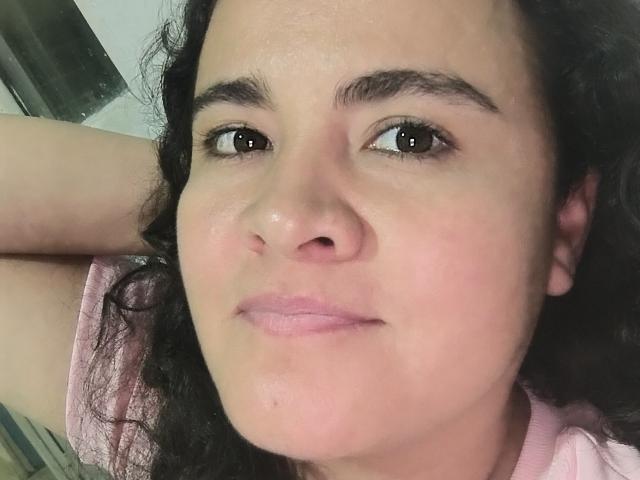 PatyHottLove's face is close-up, showing brown eyes, curly black hair, and pink lipstick. She's wearing a pink shirt with a relaxed, slightly smug expression.