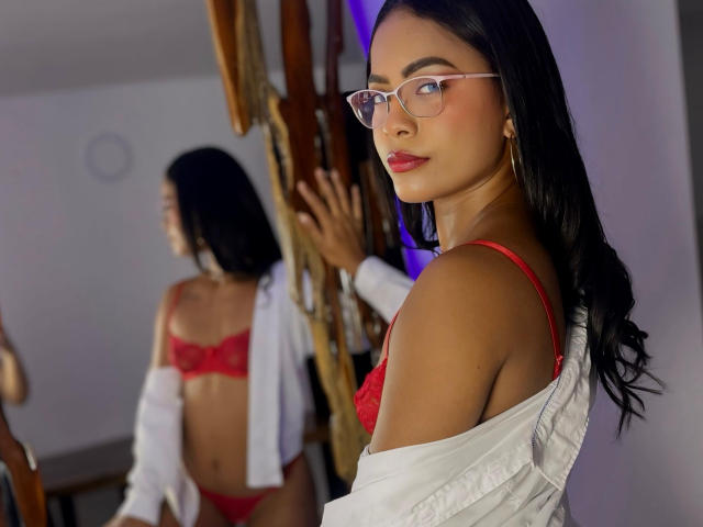 ChloeBrownOne with red lingerie, white shirt off, glasses, and long black hair, looking back at reflection showing her bare ass and red bra. Reflective wooden staircase in background.