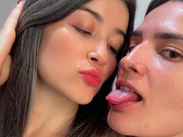 DakottaScarlett's pouty pink lips kiss a guy's tongue. She has long brown hair, pink lipstick, and a nose piercing. He has a nose ring and his tongue's out.