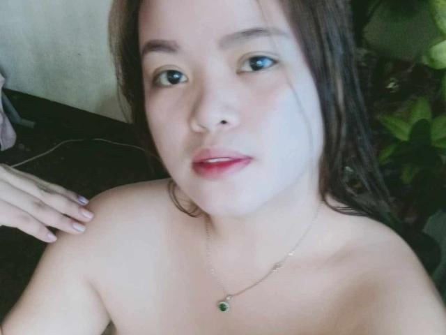 OpenMindedKinyStar with pale skin, brown hair, blue eyes, red lipstick, necklace with green gem, naked, hands on dark surface, looking at camera, slightly parted lips.