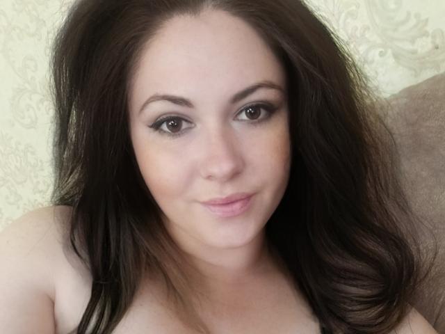 MaluskaHot has dark brown hair, brown eyes, and a slight smile. Her pale skin and subtle makeup highlight her cute face. She's topless, showing her bare shoulders.