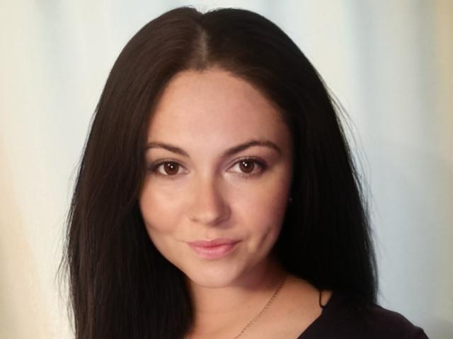 MaluskaHot has long black hair, brown eyes, and a slight smile. She's wearing a black top with a thin gold necklace. Her ass is not visible.