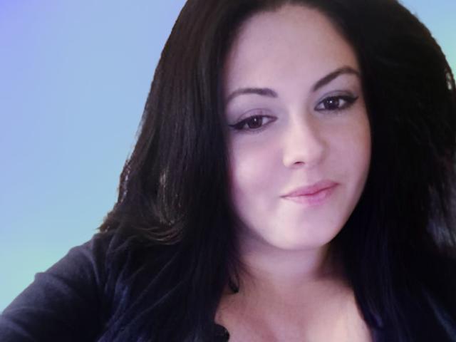 MaluskaHot with dark, wavy hair, light skin, and subtle makeup, has a slight smile and is wearing a black top, showing her small tits.
