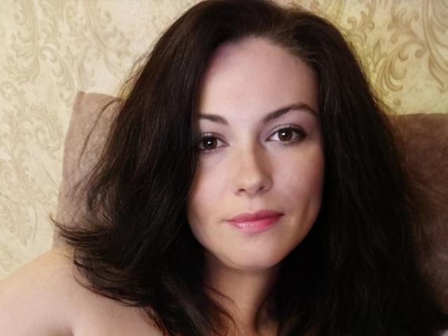 MaluskaHot has medium-length dark brown hair, brown eyes, pink lipstick, and a slightly smiling face with a subtle, confident look. She's wearing nothing, exposing her bare shoulders.