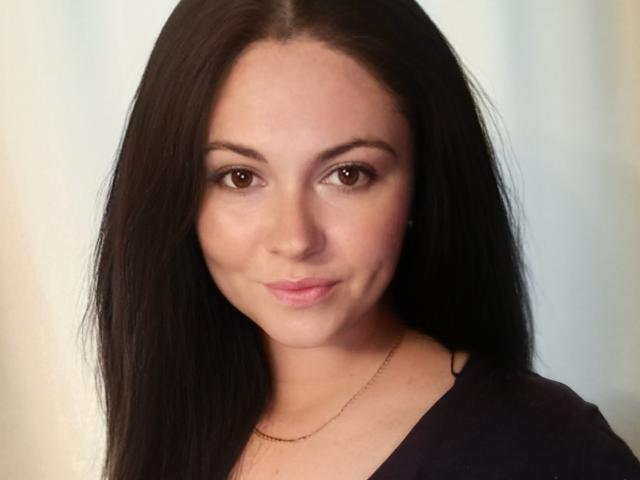 MaluskaHot has long black hair, brown eyes, light skin, subtle pink lipstick, and a small gold necklace. She's wearing a dark top, looking directly at the camera.