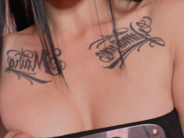 AizenMyoo has black script tattoos on her upper chest, just below her tits, reading "Britt" on the left and "Ann Marie" on the right.