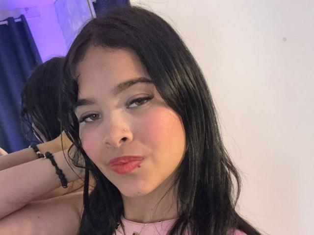 ChloeVixen with puffy pink lips, black hair, and subtle makeup, giving a pouty expression, wearing a pink top, black bracelet on her wrist, in a mirror selfie.