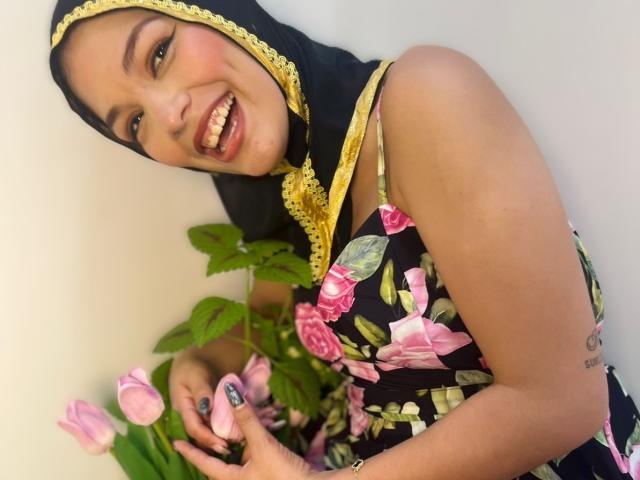 AliceKayleigh with pink floral dress, black and yellow headscarf, holding pink tulips, green leaves, looking down, smiling, fair skin, cute, soft lighting, gentle expression, small breasts, slim.