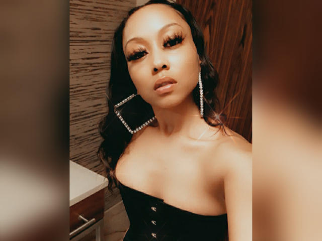 ChanelHope has dark, wavy hair, thick eyelashes, and is wearing a strapless black corset with buttons, showing her bare shoulders and small, firm tits. She's wearing large, diamond earrings.