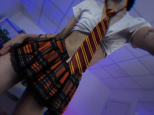 SimaWendy in a schoolgirl outfit with an orange and red plaid skirt, black lace trim, tied-up white shirt, and yellow-red striped tie, viewed from a low angle.