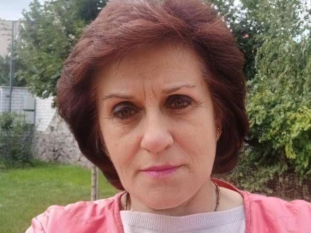 KseniaBurlesk has short brown hair, pink lipstick, and a serious expression. She's wearing a pink jacket with a white collar. Her eyes are brown and slightly squinted.