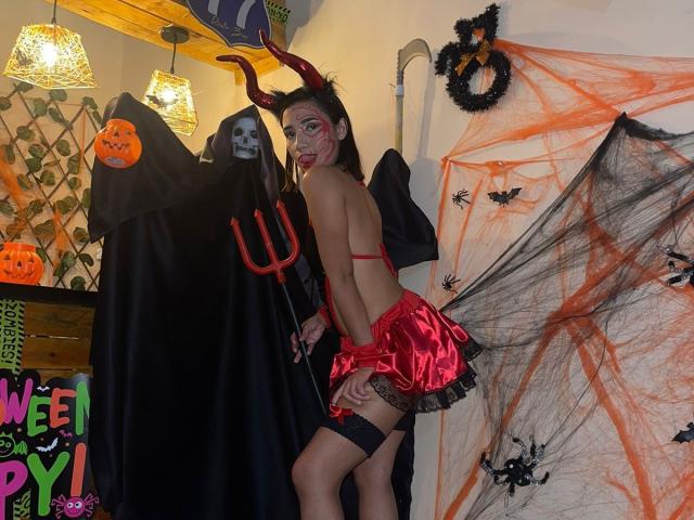TheSecretOfRoomies, verkleed als een rood duivel met hoorns, schmink en een rode rok, toont hun blote achterwerk en zwarte maillot, naast een spook met een drietand..