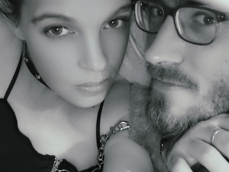 Black-and-white selfie of KevVanessHot with a woman and a man. KevVanessHot has glasses, beard, and mustache. Woman has small tits, chain necklace, and serious expression.