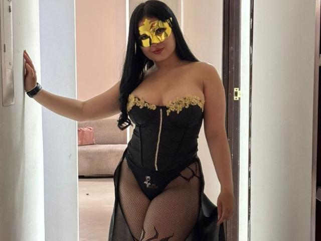 LunaBellaHotty with black corset, gold lace, fishnet legs, and golden mask, standing in doorway, showing her curvy tits and pussy through the mesh, long black hair.