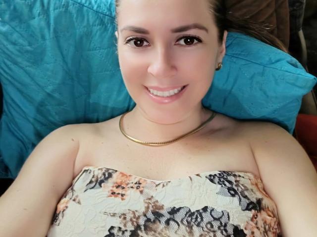 Jammyx69 has light skin, brown eyes, and a smile, wearing a floral strapless top, lying on a blue pillow, with brown hair and a gold necklace.