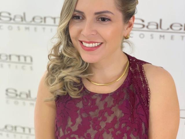 Jammyx69 with blonde curls, red lipstick, and a lace sleeveless dress, smiling at the camera, wearing gold earrings and a gold necklace, looking cute and sexy.