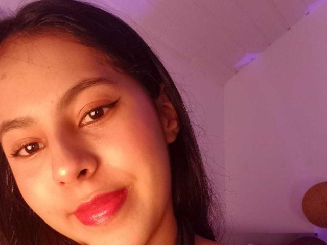 SoffiRousee's face with dark hair, brown eyes, and red lips, wearing black eyeliner, smiling slightly, in soft purple lighting, showing smooth skin and a cute, pretty look.
