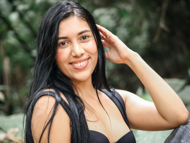 SaraRousse has long black hair, a cute smile, and is wearing a black top, showing her small tits, with a hand in her hair, looking cute and sexy.