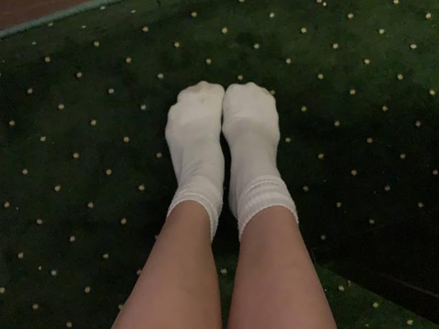 MoonLiza's legs in white socks, feet touching, on green carpet with small yellow dots. Socks are slightly dirty at the toes. Shot from above.