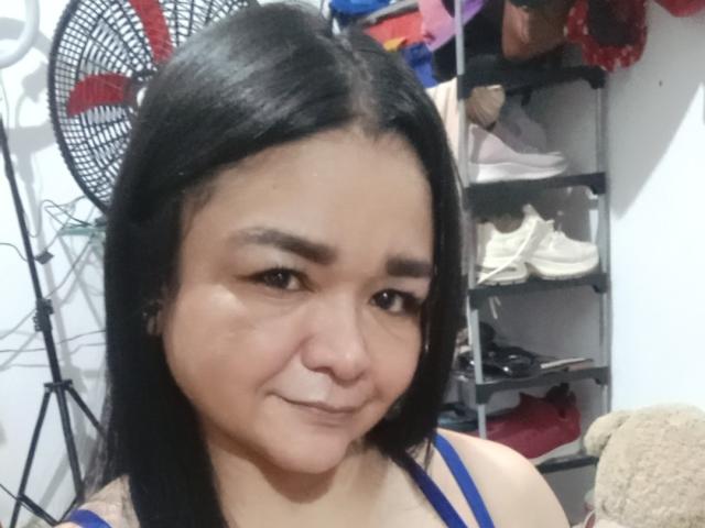 TinaMarcia with black hair, brown eyes, and a slight smile, wearing a blue strap, showing her cute face and small nose. Her tits are not visible.