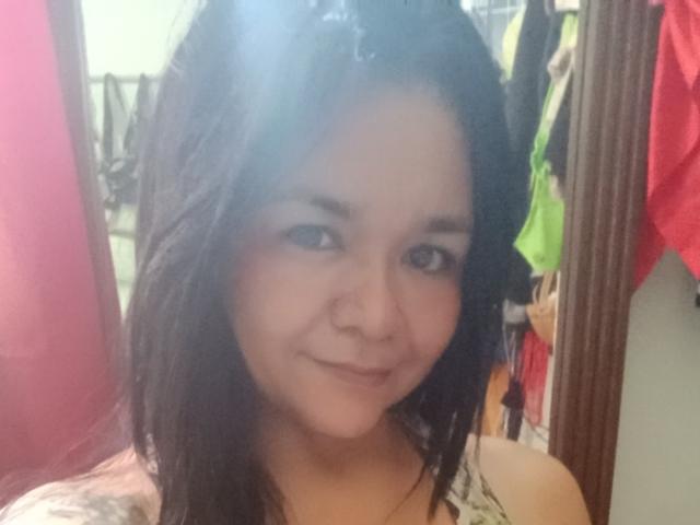 TinaMarcia has black hair, brown eyes, and a small nose ring. She's smiling with a light skin tone, wearing a patterned top. Her tits are partially visible.