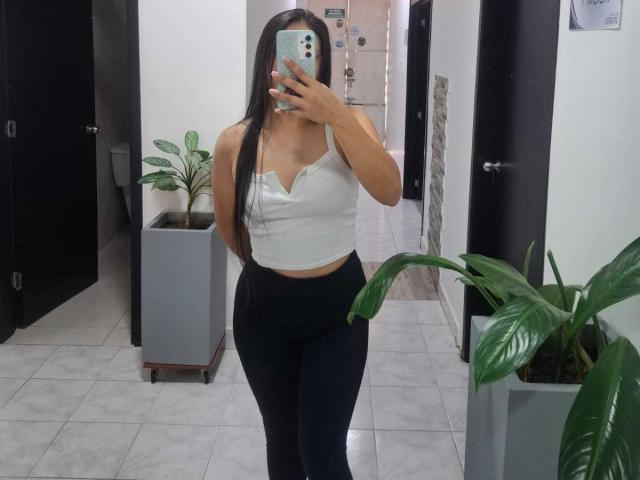 AnnieHill with long black hair, wearing a white tank top and black high-waisted leggings, showing her tits and ass, taking a mirror selfie in a room.