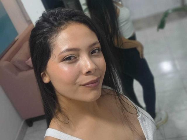AnnieHill with dark wet hair, light brown skin, small nose, subtle smile, wearing a white off-shoulder top, visible reflection showing her back and ass in the mirror.