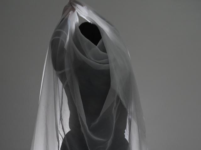 CherylSweetX is a dark silhouette with a translucent white cloth wrapped around her head and torso, creating a mysterious, ghost-like appearance. Her arms are raised, holding the cloth.