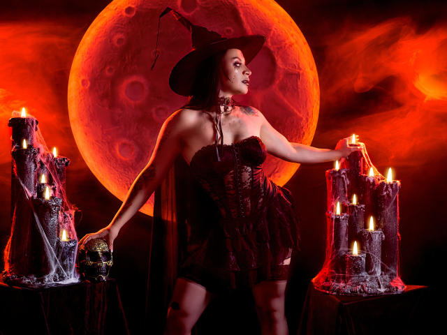 KatalinaJohnson in a dark witch outfit, standing with a witch hat, holding a skull, arms around glowing candles, moon in background, red-orange sky, black lingerie, sexy, curvy.