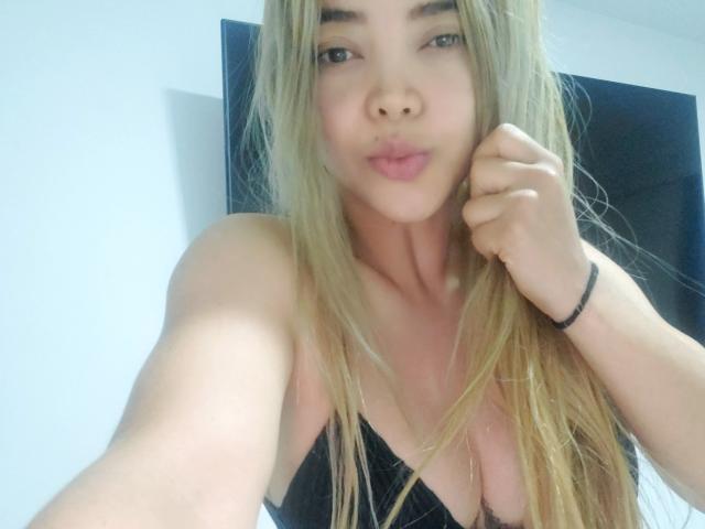 SalomeKiki69 has long blonde hair, pouty pink lips, and is wearing a black top with visible cleavage. She's taking a selfie, holding her hair with one hand.