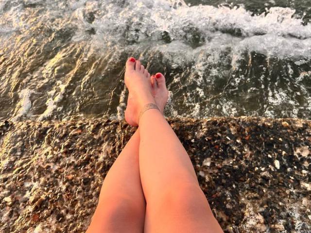 Diamond69s aveva le gambe incrociate alla caviglia, le dita dei piedi con lo smalto rosso, una cavigliera alla gamba destra, in piedi in acque poco profonde con piccole onde..