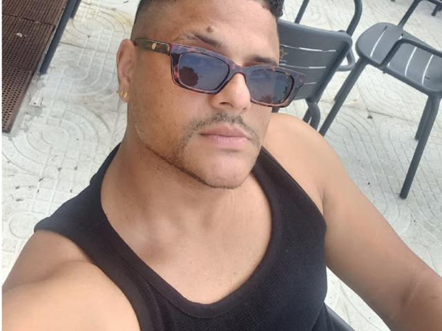 TheHottLover ha una corporatura muscolosa, indossa una canotta nera e occhiali da sole marroni a tartaruga, con un orecchino dorato e un taglio di capelli corto e riccio. Il suo viso è leggermente abbronzato..