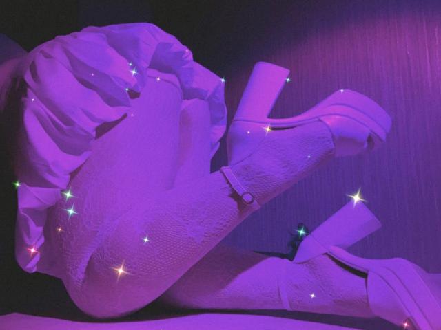 RomanMoore's purple-lit legs in textured tights, wearing high platform heels with ankle straps, crossed at the knees. Glittering star effects are scattered across her legs.