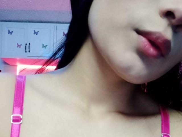 Marbela's face, showing her pink bra straps, with her plump lips slightly parted, her fair skin, and dark hair. Her small gold earrings are visible.