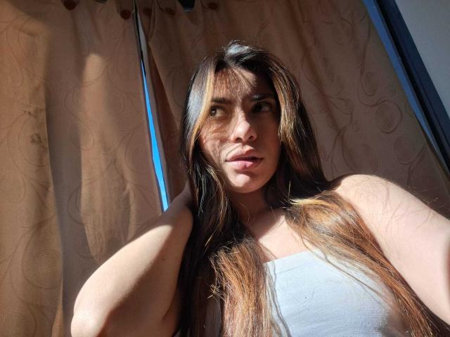 AmaiaSalvatoree with long brown hair, sunlight in her eyes, wearing a white strapless top, hand in hair, looking to the side, soft shadow on her face.