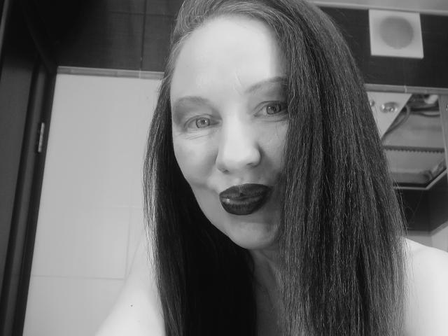 Black-and-white selfie of DashaHart with long dark hair, pale skin, dark lipstick, and a slight smile. Her eyes are centered, and she's topless with bare shoulders visible.