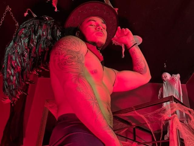 Muscular JeisonStark with tattoos, wearing a cowboy hat, holding a chain, red light, shirtless, dark pants, and a creepy doll in the background, looking intense.