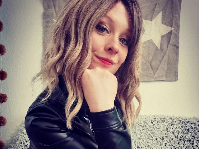 Annekehot-sex with wavy blonde hair, black leather jacket, and red lipstick, resting her chin on her hand, smiling slightly. Her hand is on her face, showing her ass.