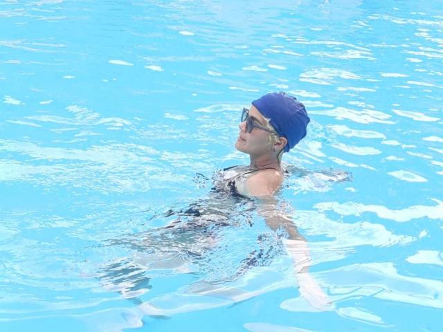 AnaRoa is in the pool, wearing a blue cap and dark sunglasses, with her tits barely visible above the water. Her ass is partially submerged.