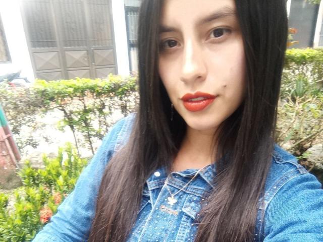 MadissonFontaine with long black hair, red lipstick, and blue denim shirt, showing her cute face and small beauty mark near her mouth. Her tits are slightly visible.