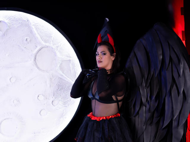 ElizabethDupont with black wings, red headband, sheer top showing her tits, black gloves, and black skirt with red trim, standing next to a giant moonlit circle.