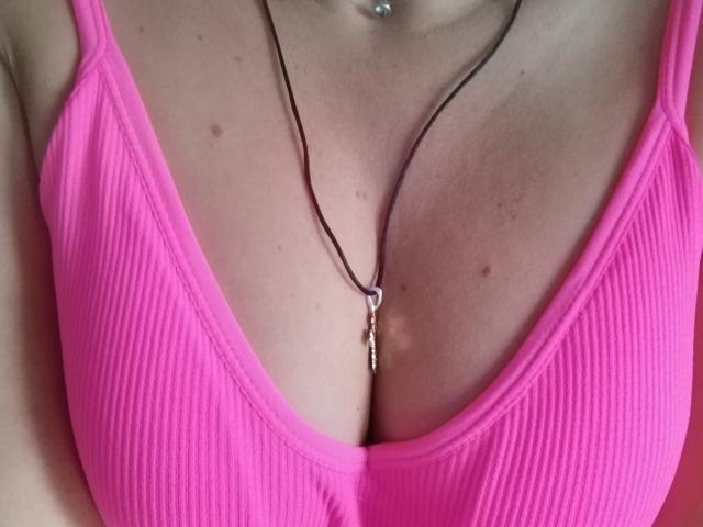 MarleneFan's pink ribbed tank top with a deep V-neck, showing her large, pale, cleavage-filled tits. She has a thin necklace with a small pendant.