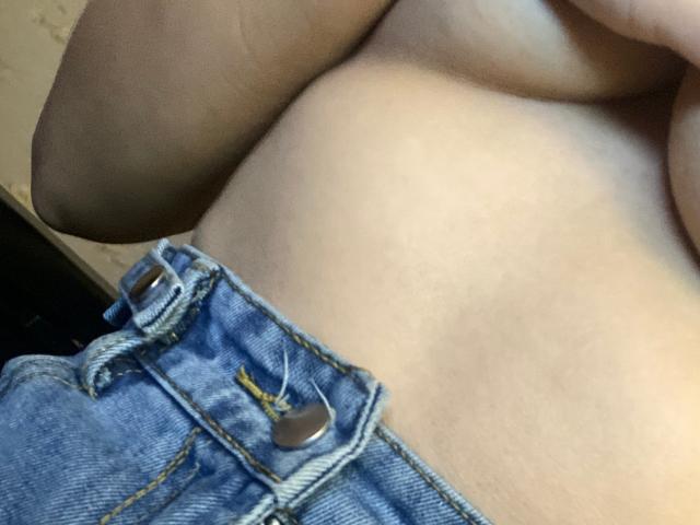 A topless SexLoveDuo with bare, pale skin showing a soft belly, wearing unbuttoned blue denim jeans with metal buttons. Their arm is partially visible on the left.