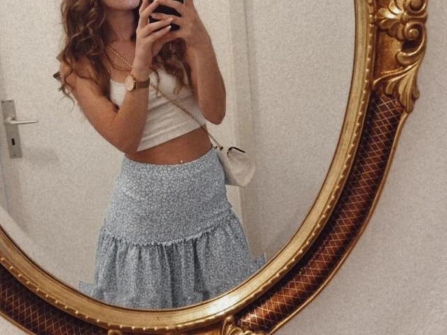Leilaaa-hot with wavy brown hair, white crop top, and blue floral skirt, holding phone, mirror reflection, gold ornate frame, white purse, soft belly, wrist bracelet.