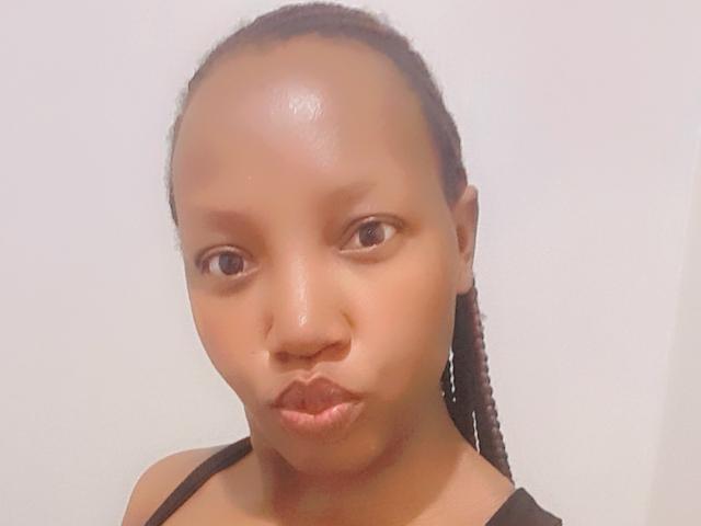 RinaAri with brown skin, small nose, and braided hair, pouting her glossy lips, wearing a black top, in a selfie.