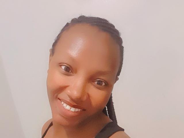 RinaAri has shiny brown skin, small brown eyes, and a big smile showing white teeth. She's wearing a black top with braids pulled back.