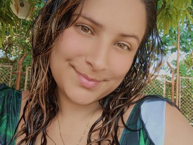 Marcee69 has wet brown hair, a cute smile, and brown eyes, wearing a green and blue top, with a gold necklace, looking directly at the camera.